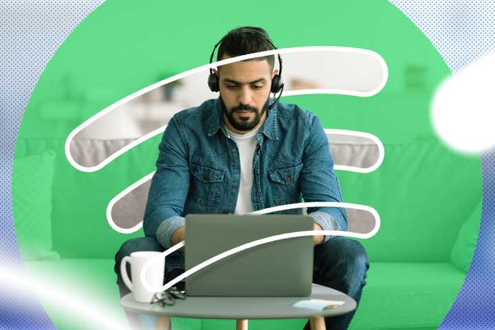A serious man working on his laptop wearing headphones with the Spotify logo in the background.