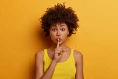 Young woman on a colorful background with a finger to her mouth in a shush motion.