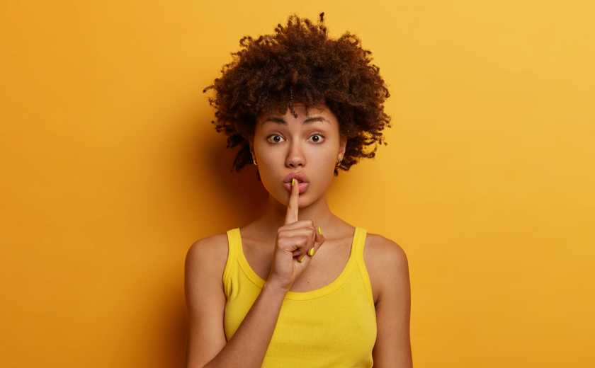 Young woman on a colorful background with a finger to her mouth in a shush motion.