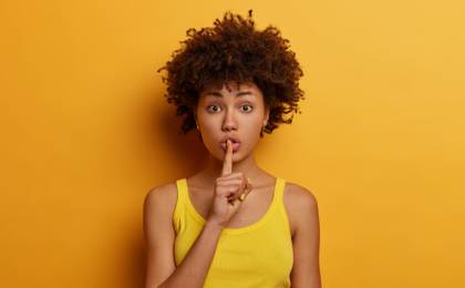 Young woman on a colorful background with a finger to her mouth in a shush motion.