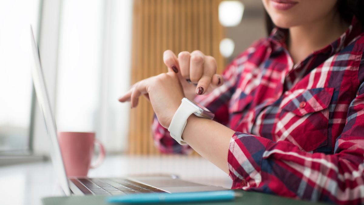 A woman looking at a white smartwatch on her wrist.