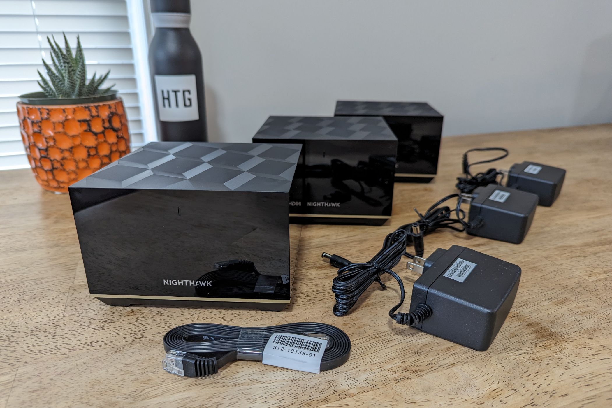 Box contents of the Netgear Nighthawk MK93S Tri-Band Mesh Wifi 6E System arranged in a row on a table.