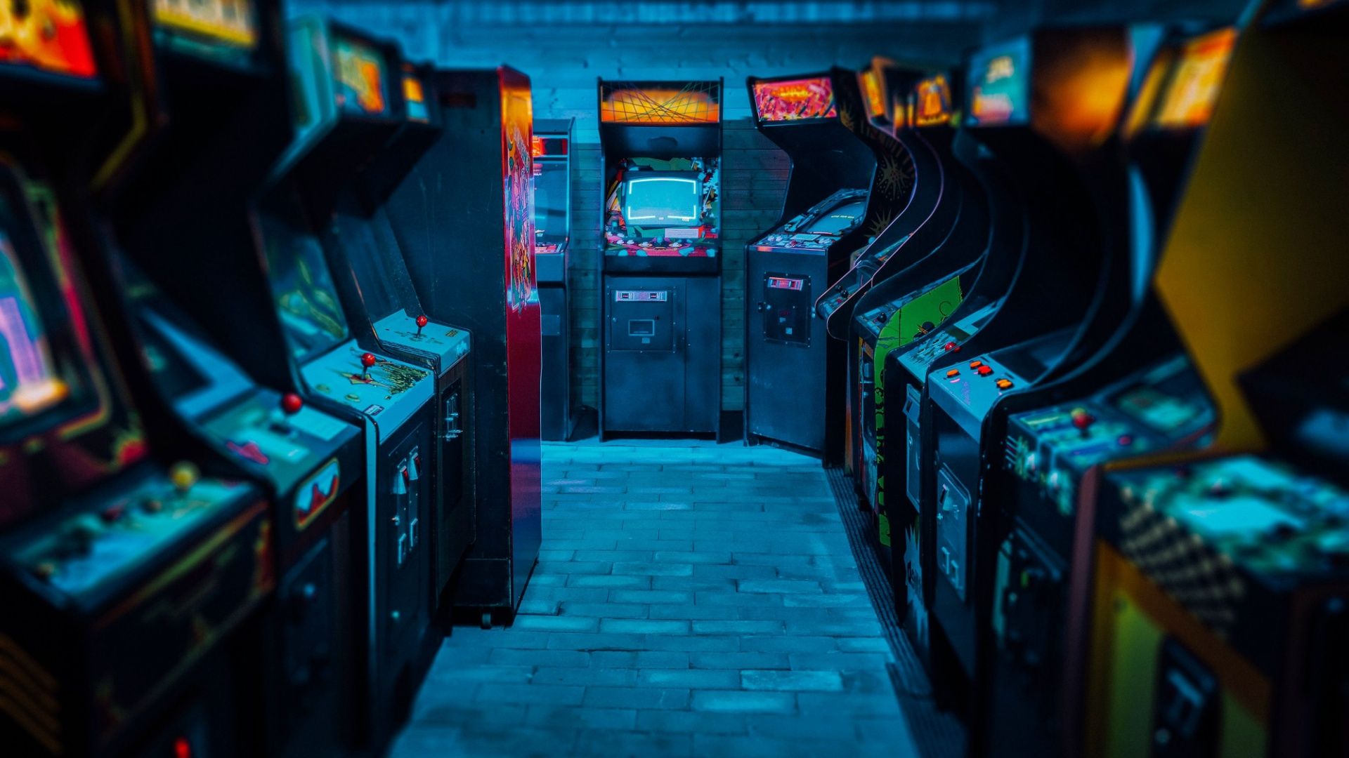 Old Vintage Arcade Video Games in an empty dark gaming room with blue light with glowing displays and beautiful retro design.