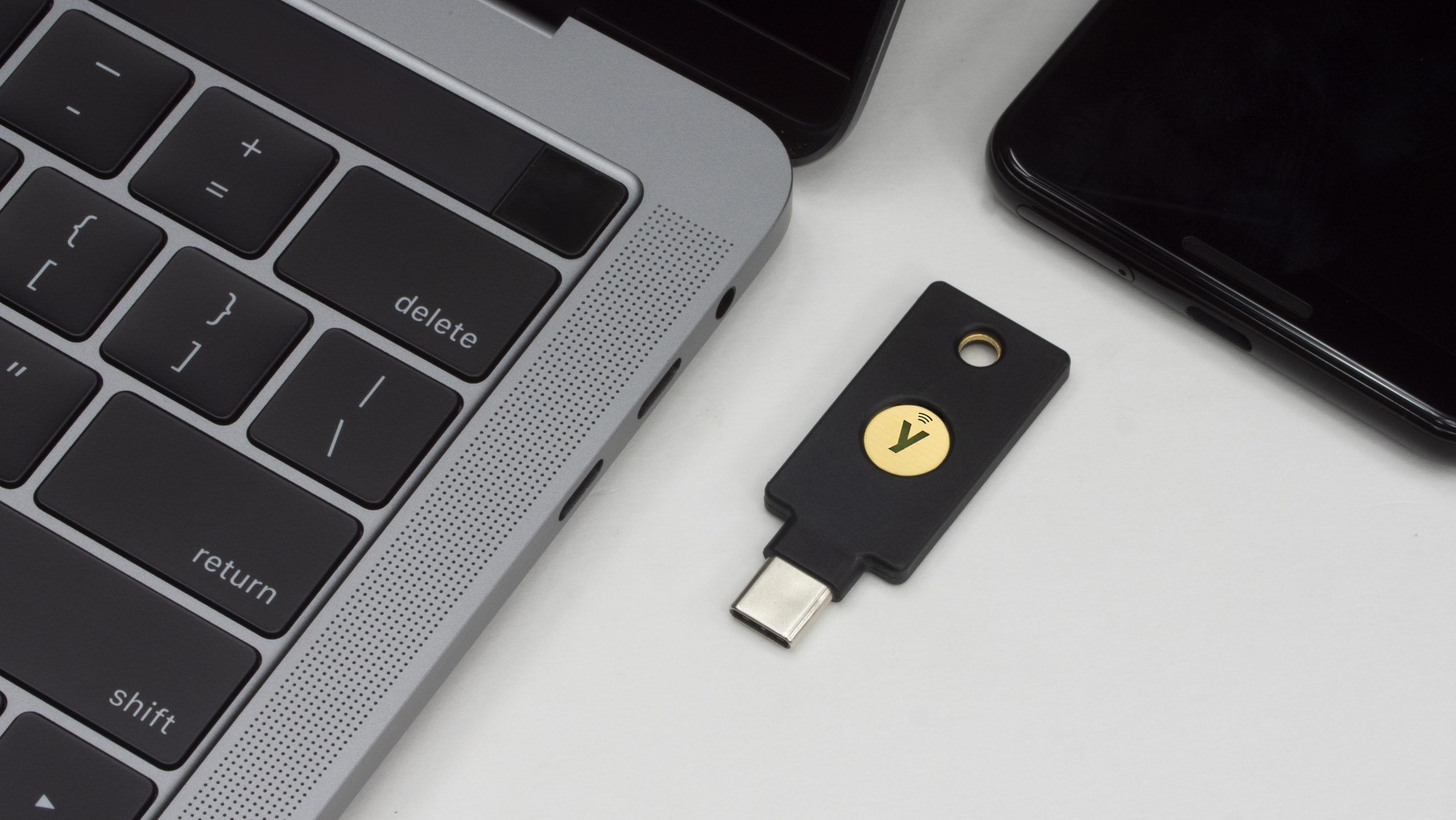 A YubiKey 5C NFC security dongle next to a MacBook and Android phone.