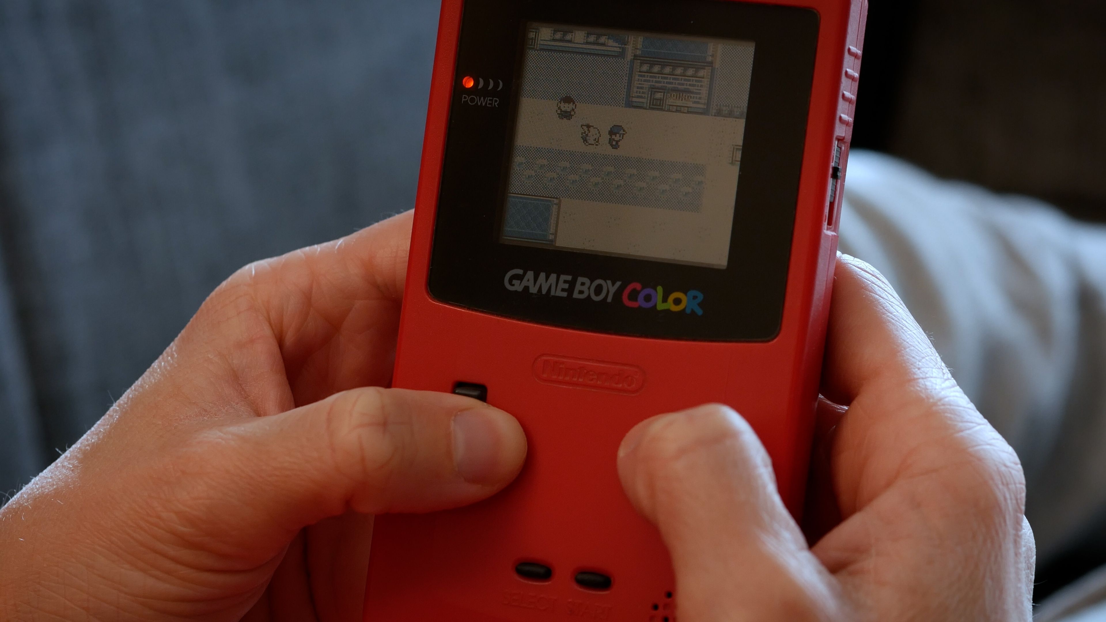 A person playing Pokemon on a Game Boy Color.
