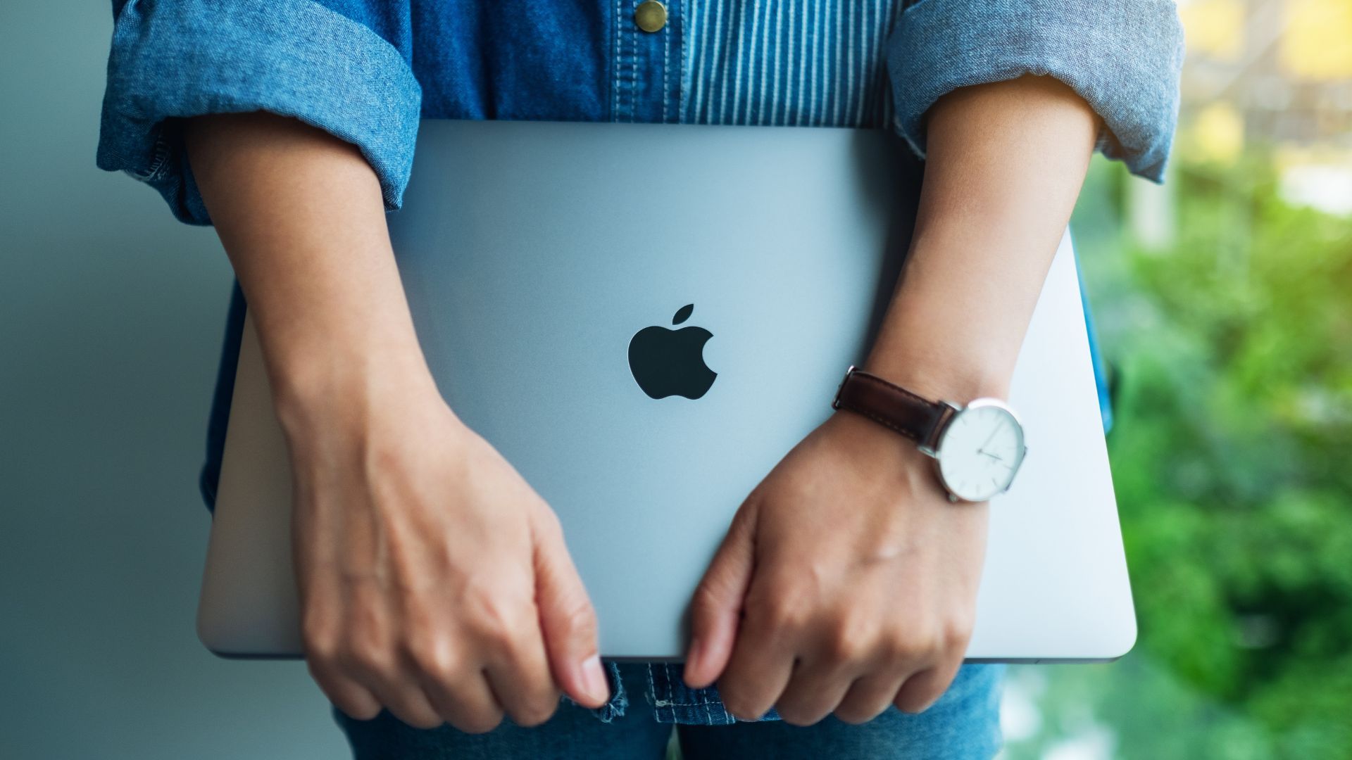 A woman standing and holding an Apple MacBook Pro laptop computer.