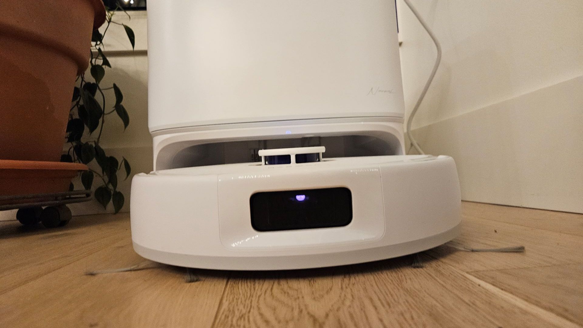 A white robot vacuum exiting its docking station on a wooden floor.