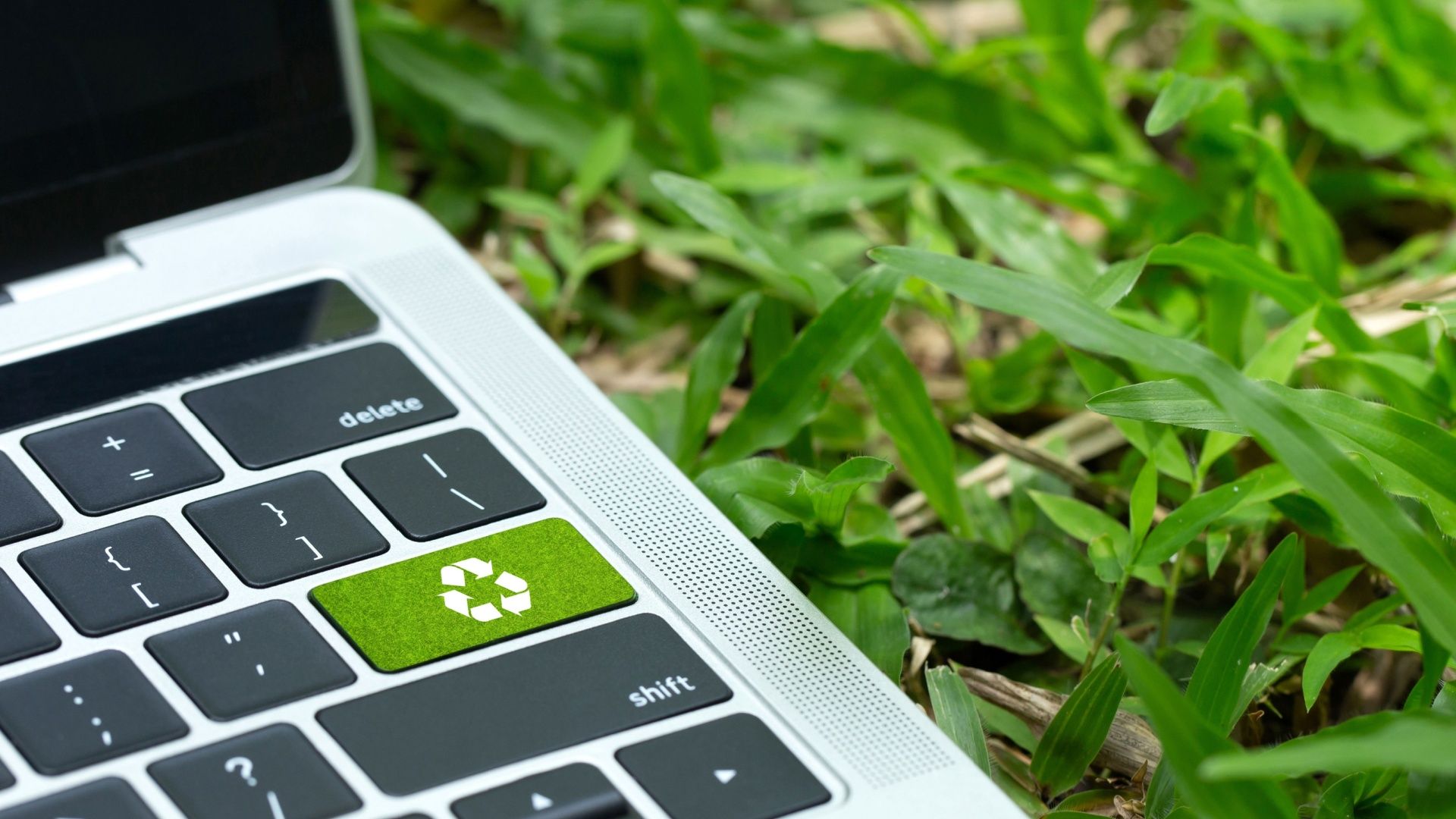 A MacBook on grass with a green recycle button where Enter should be.