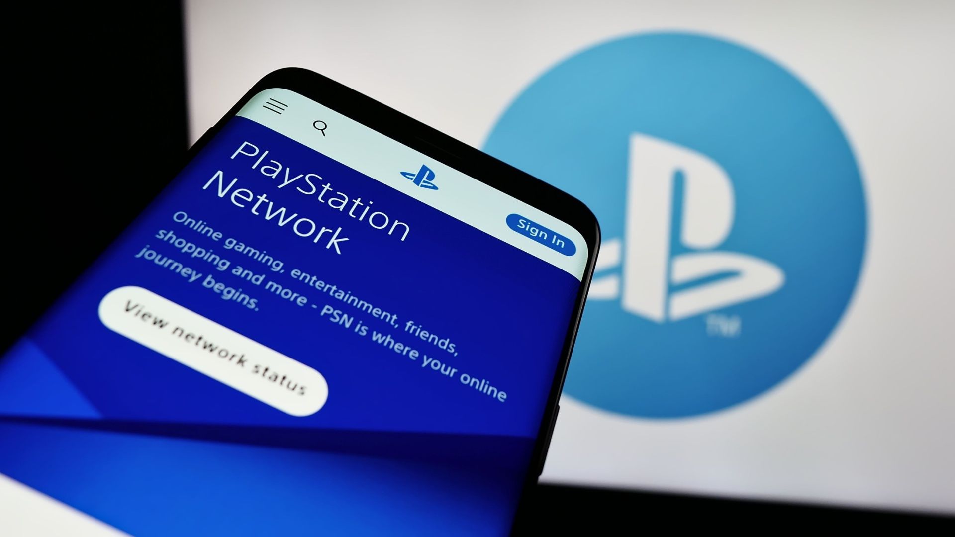 Smartphone with website of video gaming platform PlayStation Network (PSN) in front of business logo.