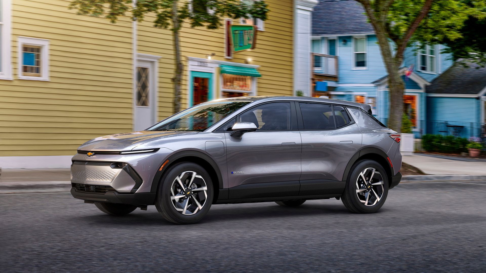Dynamic side profile shot of a gray 2024 Chevrolet Equinox EV 1LT driving through a city.
