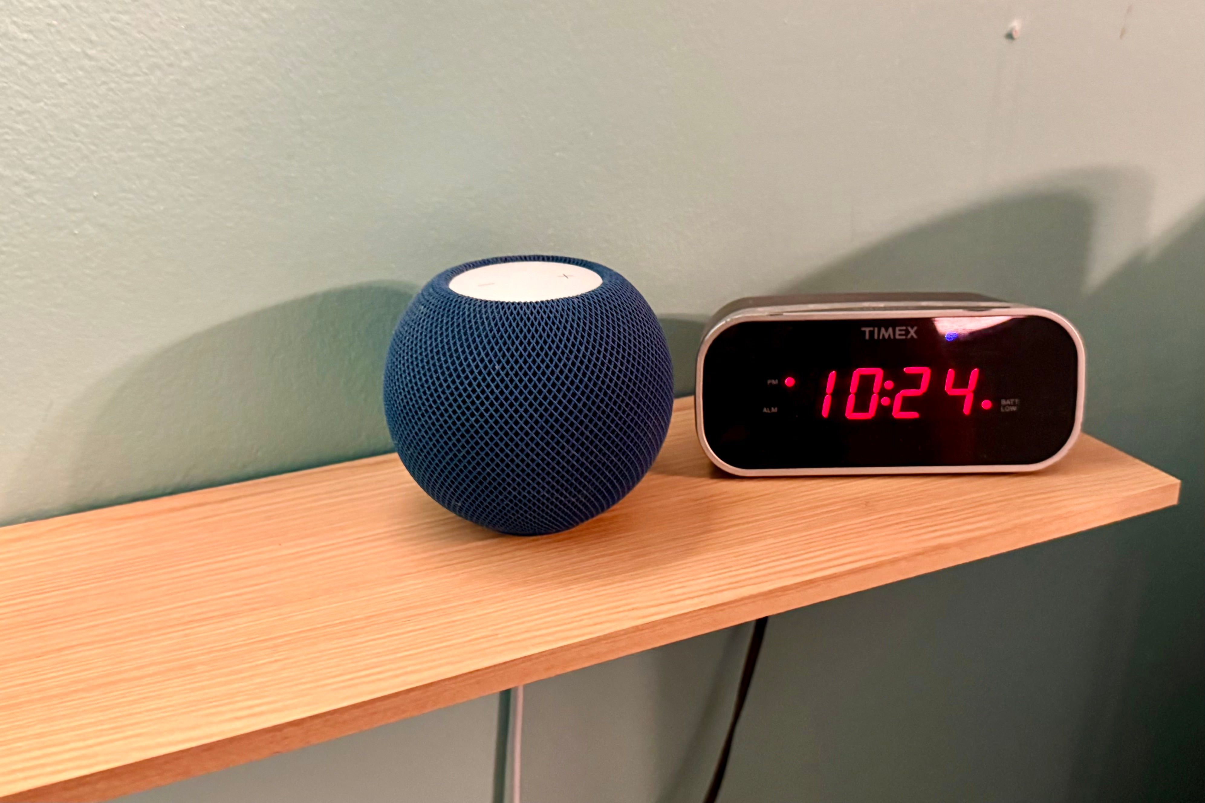 HomePod mini on a shelf next to a digital clock.