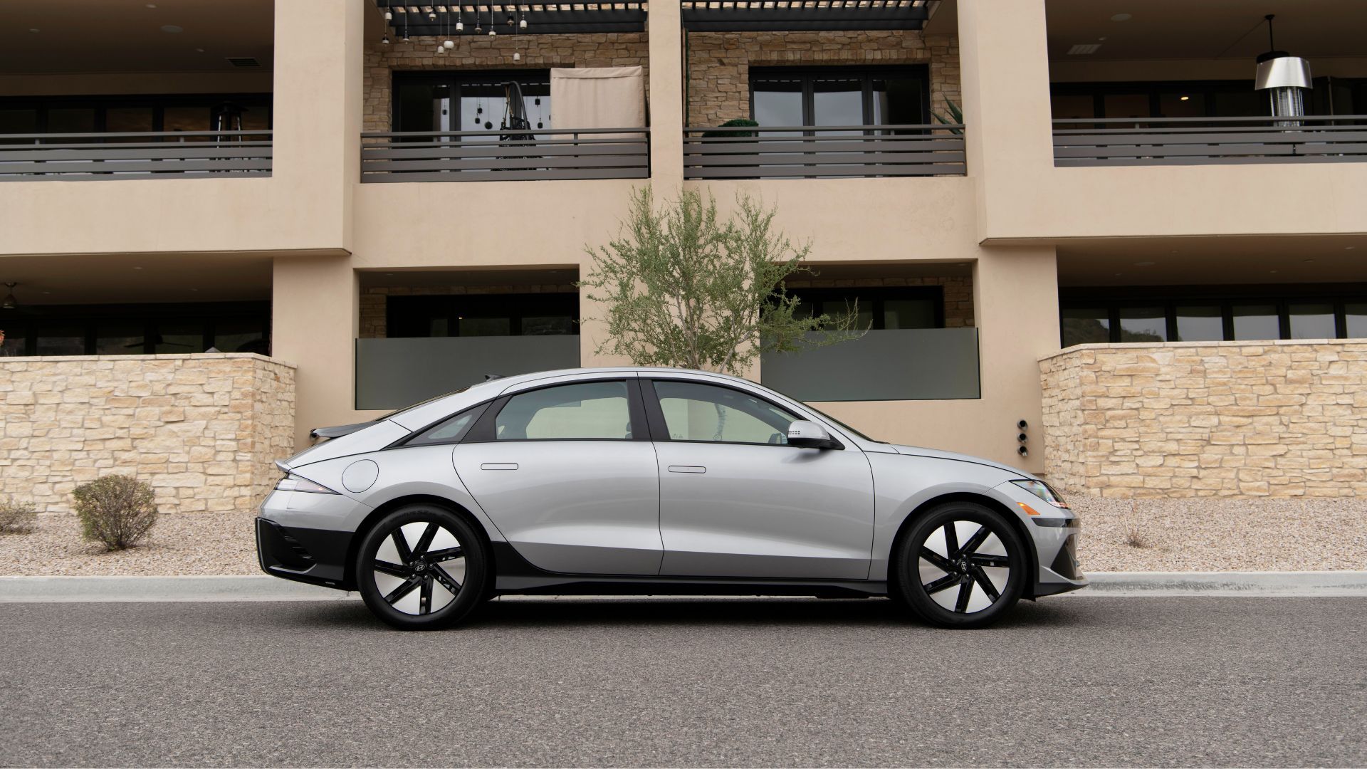 Static side profile shot of a silver 2025 Hyundai Ioniq 6 SE parked outside of a residential building.