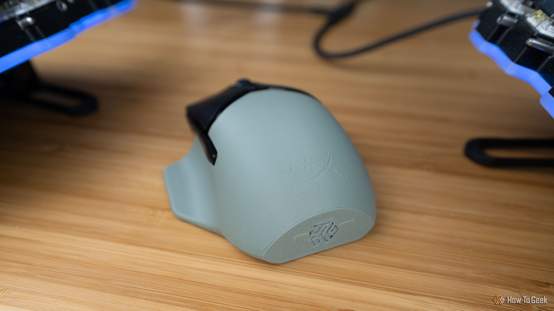 The back of the HyperX Pulsefire Saga Pro wireless gaming mouse with a custom 3D printed shell with the How-To Geek logo embossed on it..
