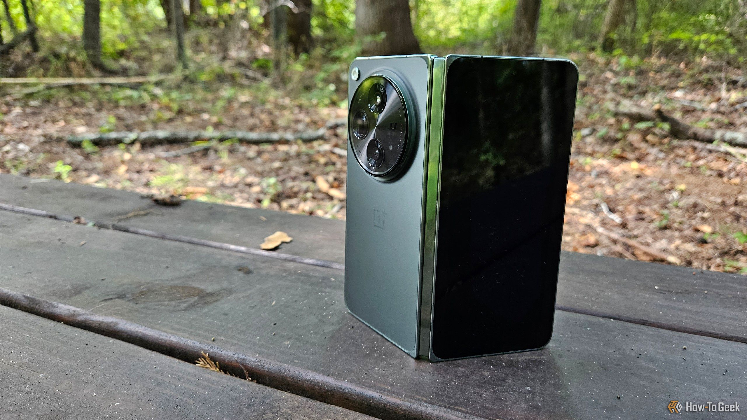 OnePlus Open on a wooden bench in the woods.